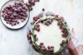 A cranberry wreath cake on a granite cake platter with a small plate of sugared cranberries next to it.