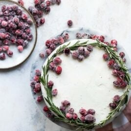 A cranberry wreath cake on a granite cake platter with a small plate of sugared cranberries next to it.