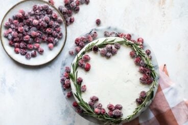 A cranberry wreath cake on a granite cake platter with a small plate of sugared cranberries next to it.