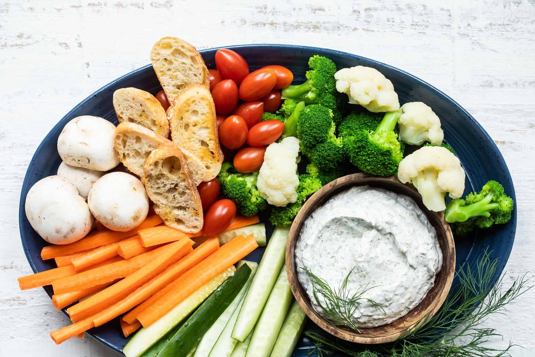 A platter with dill dip and fresh vegetables.