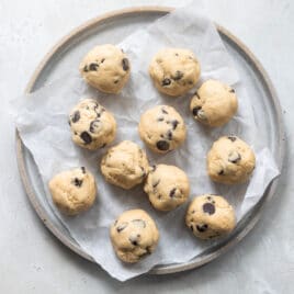 Balls of chocolate chip cookie dough on a plate before freezing.