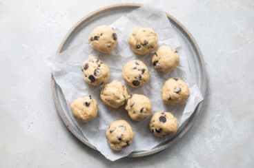 Balls of chocolate chip cookie dough on a plate before freezing.
