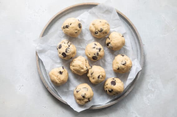 Balls of chocolate chip cookie dough on a plate before freezing.