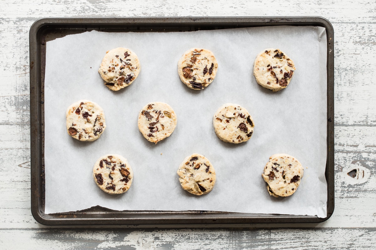 Baked fruitcake cookies on a parchment paper lined baking sheet.
