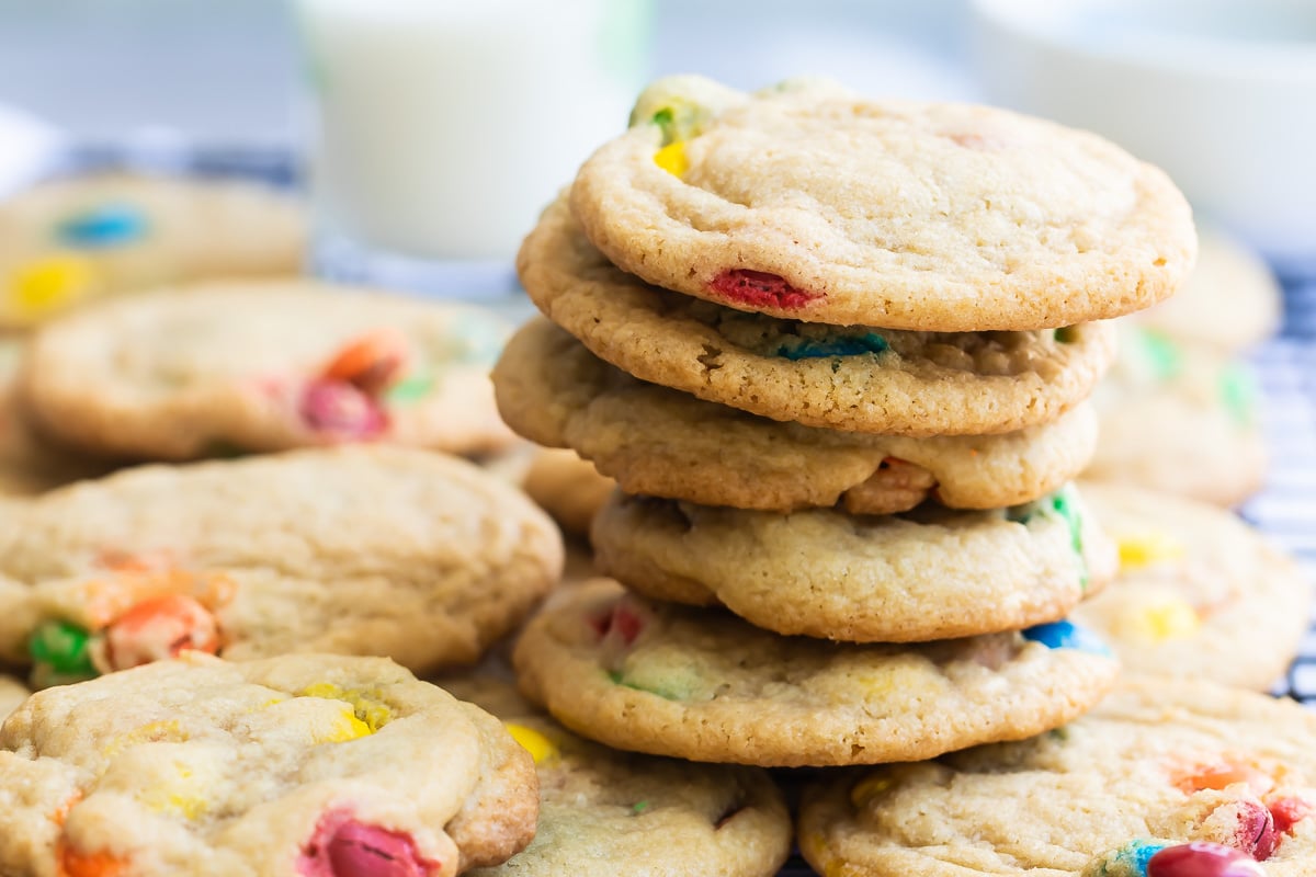 A stack of M&M cookies on a cooling rack.