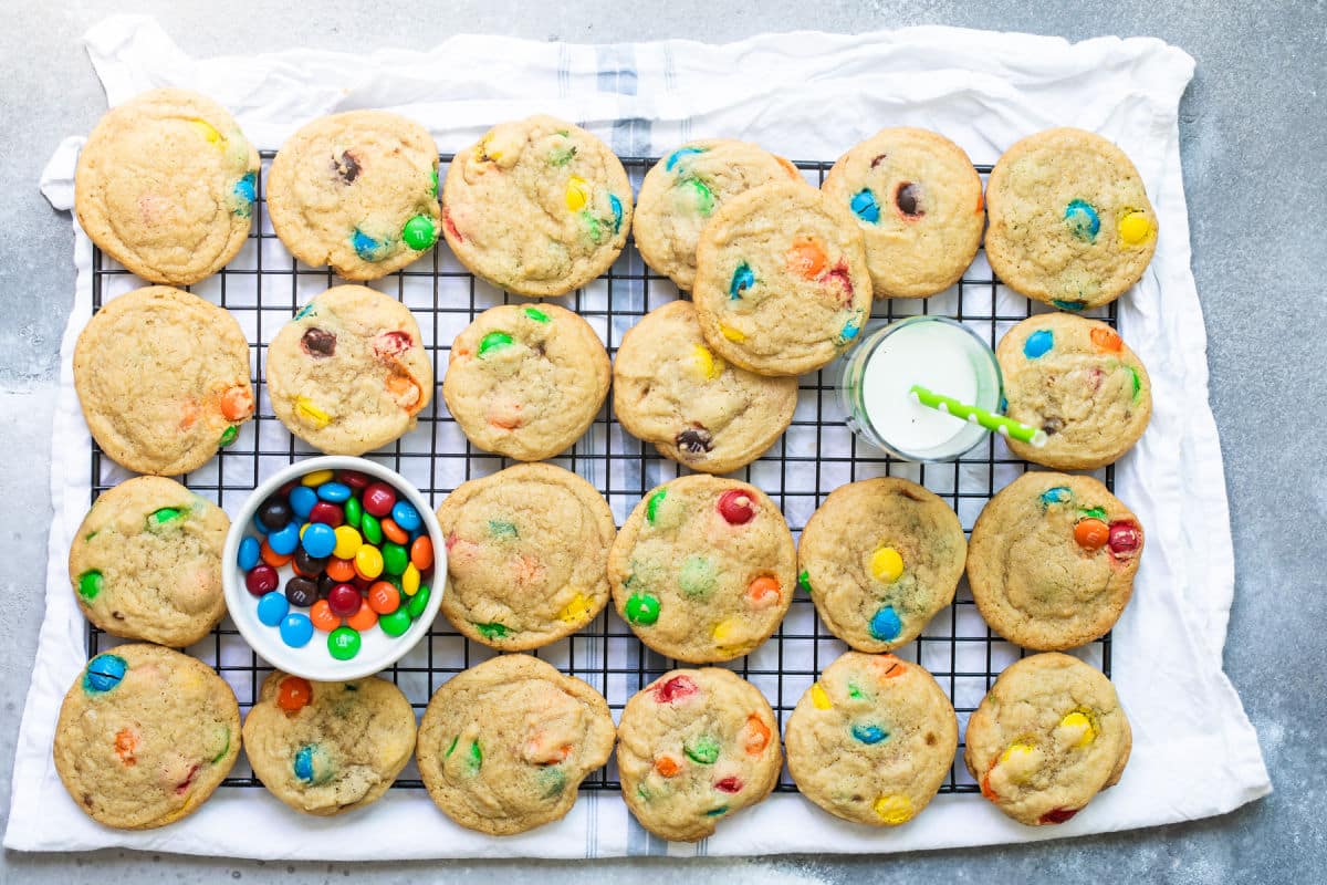 A batch of M&M cookies on a cooling rack.