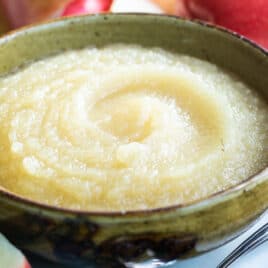 A bowl of applesauce with apples behind it.