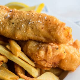 Beer battered cod, fries, tartar sauce and a lemon wedge on a plate.