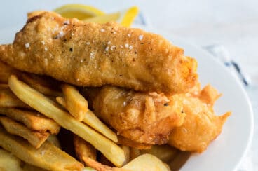 Beer battered cod, fries, tartar sauce and a lemon wedge on a plate.