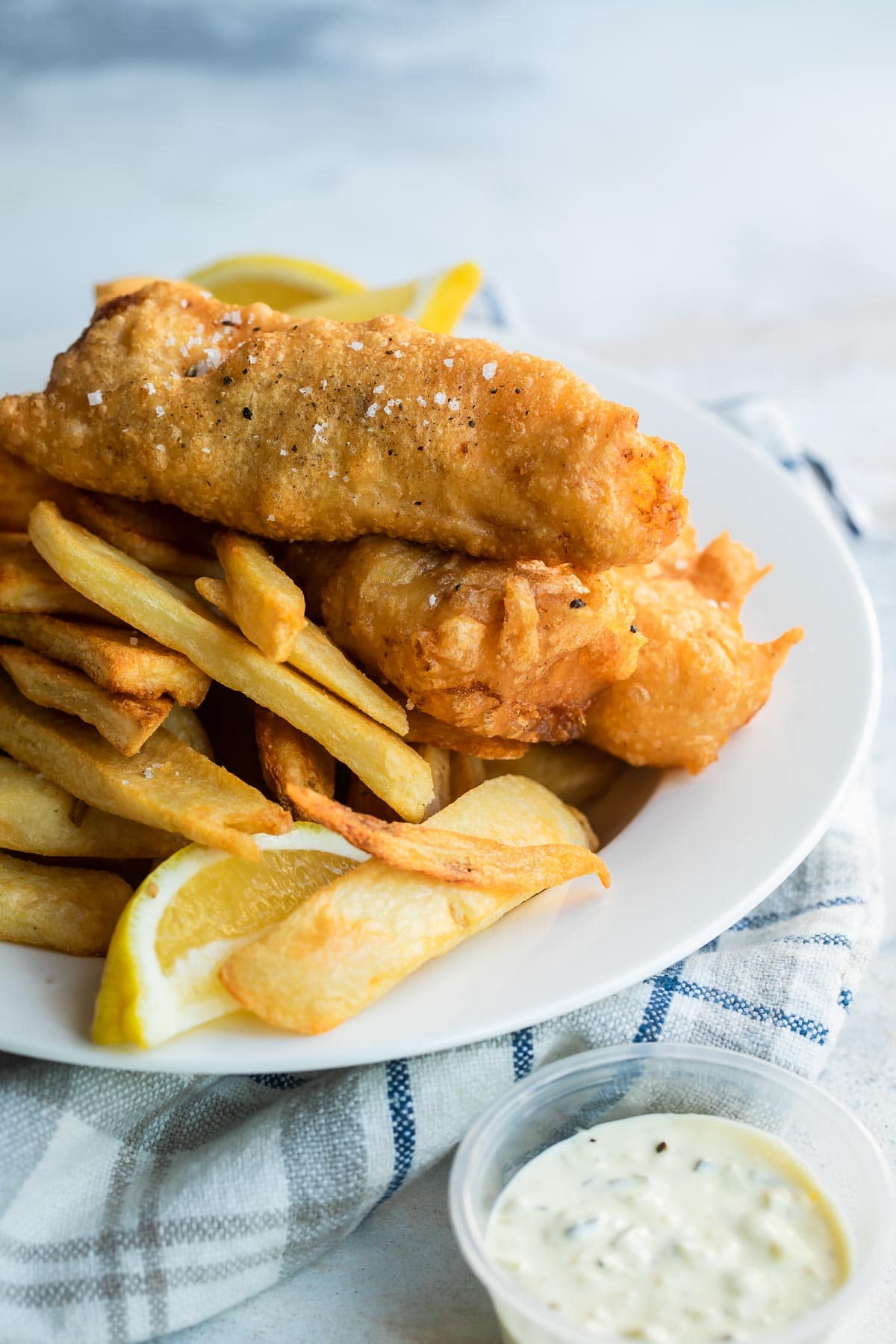 Beer battered cod, fries, tartar sauce and a lemon wedge on a plate.