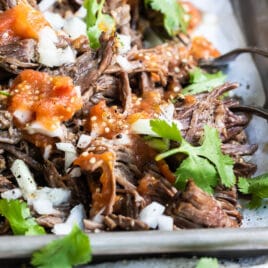 Garnished birria on a silver baking sheet.