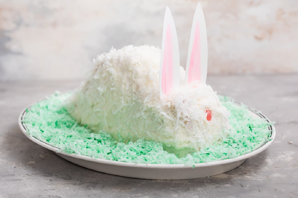 A bunny cake on a bed of green coconut on an oval plate.