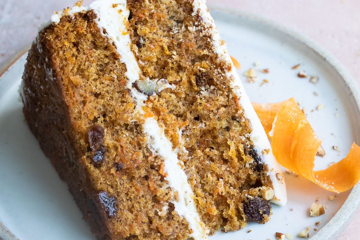 A slice of carrot cake on a blue plate with a candied carrot peel.