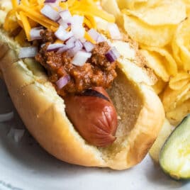 A chili dog on a plate with a pickle and chips.