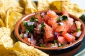 Chipotle tomato salsa in a black bowl on a blue plate with tortilla chips.