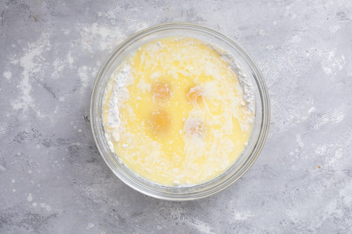Wet ingredients for cornbread in a clear glass bowl before being mixed.