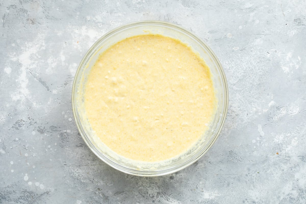 Wet ingredients for cornbread in a clear glass bowl after being mixed.