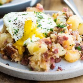 Corned beef hash on a gray plate topped with and egg and parsley.