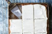 Banana bars with cream cheese frosting in a pan with a spatula for serving.