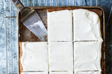 Banana bars with cream cheese frosting in a pan with a spatula for serving.