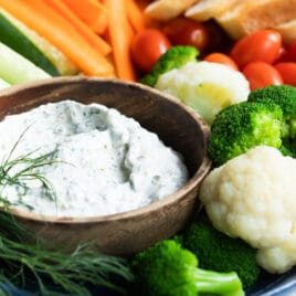 A platter with dill dip and fresh vegetables.