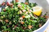 Bulgar tabbouleh in a white bowl with a lemon garnish.