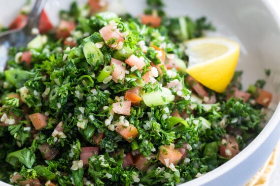 Bulgar tabbouleh in a white bowl with a lemon garnish.