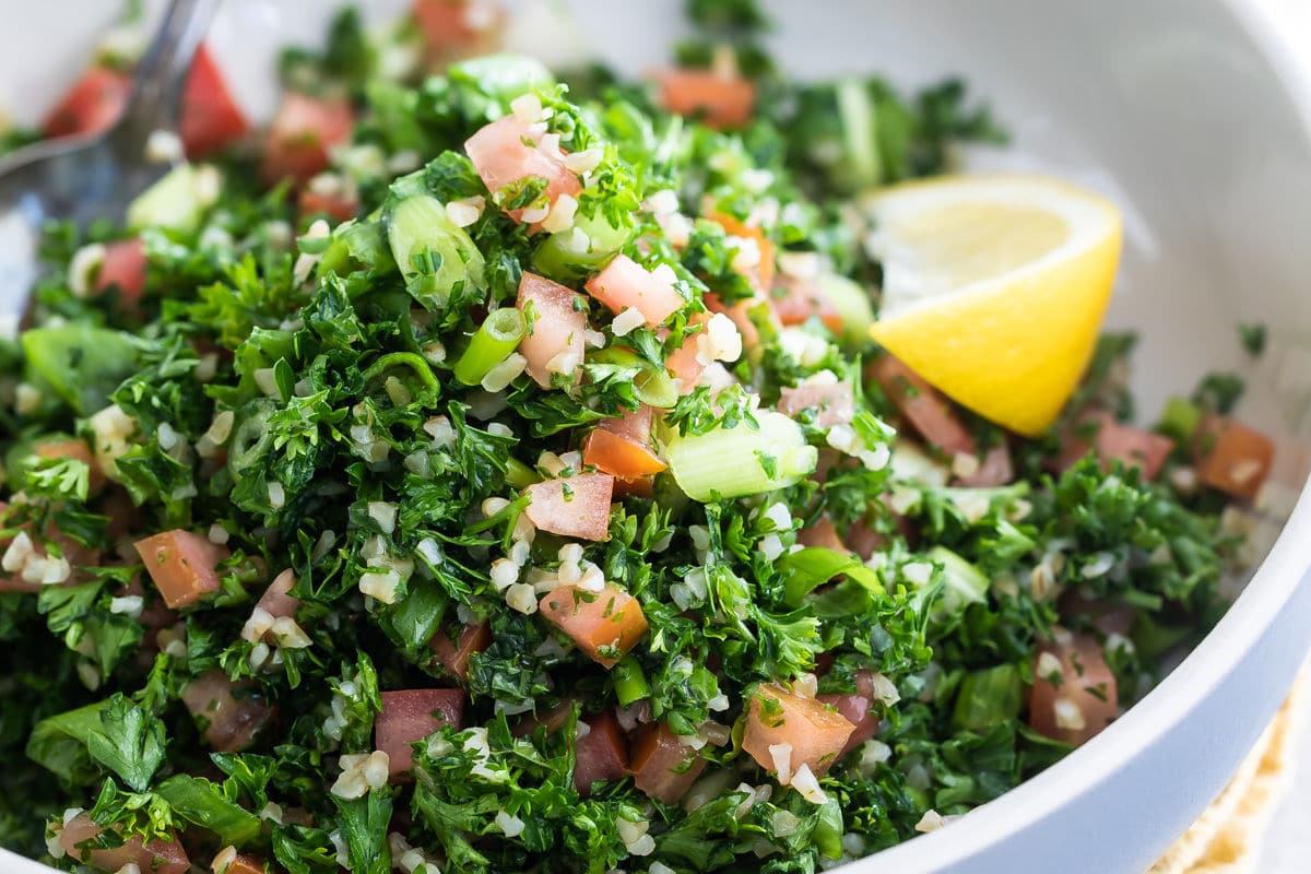 Bulgar tabbouleh in a white bowl with a lemon garnish.