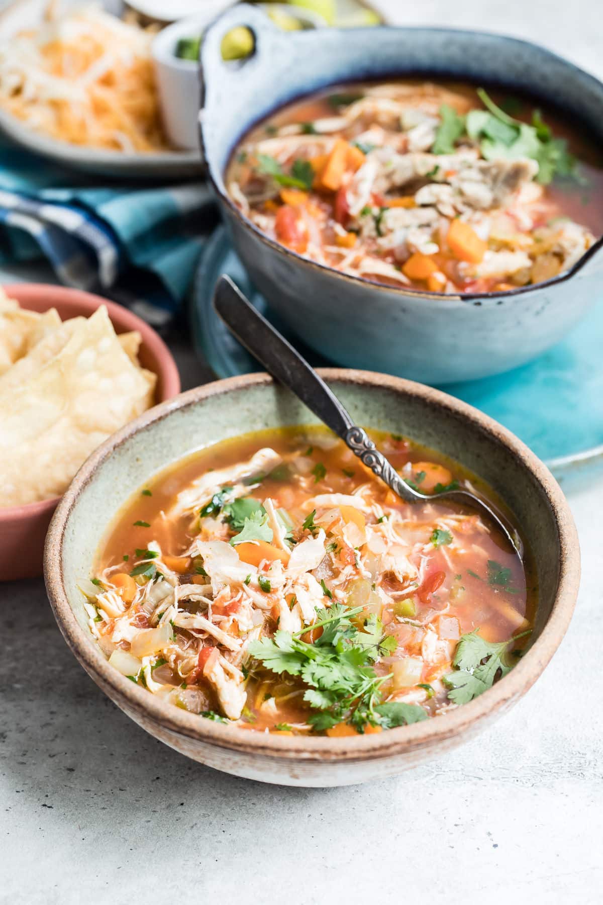 Two bowls of Mexican chicken soup with toppings nearby.