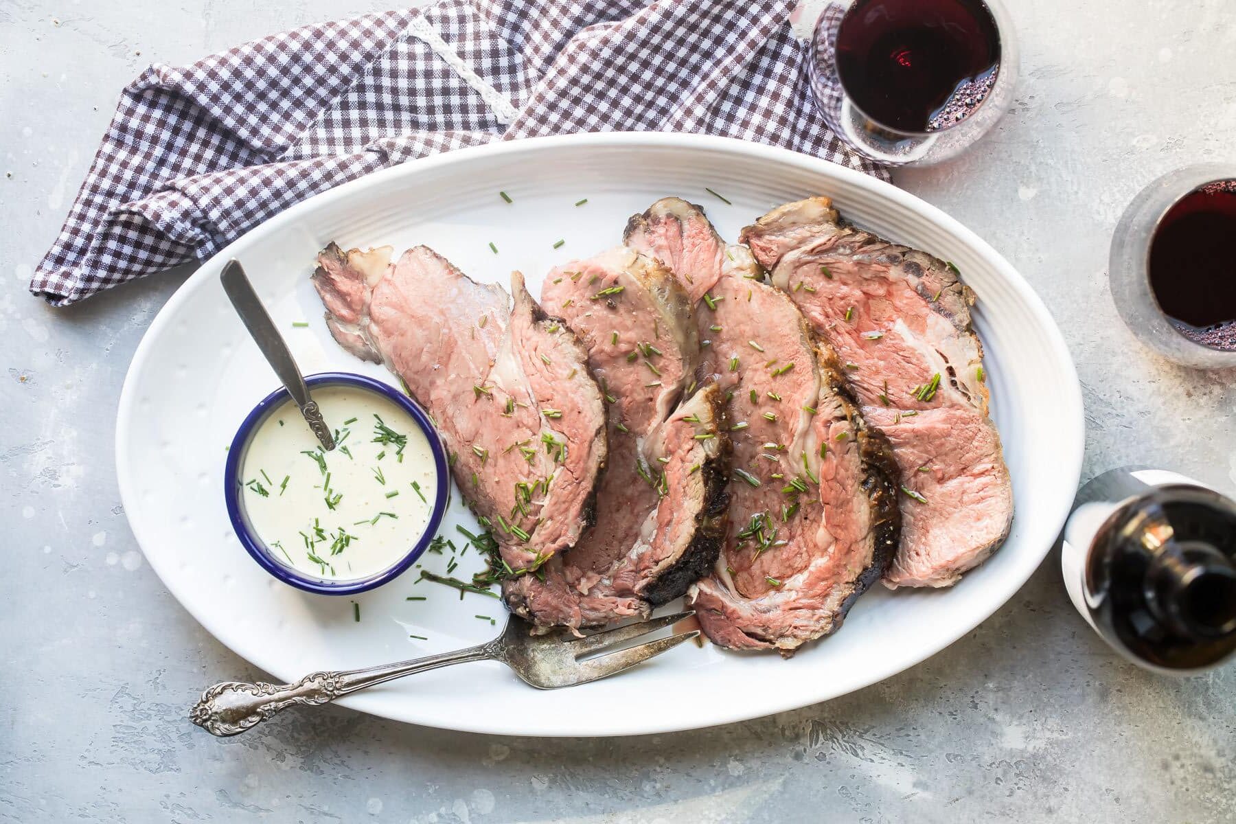 A platter with sliced prime rib next to a small cup of mustard cream sauce.