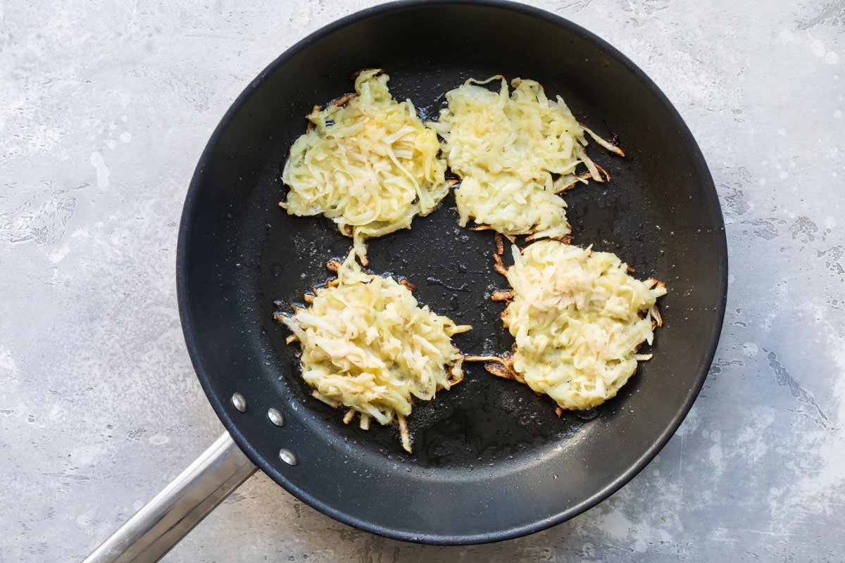 4 potato latkes frying in a pan.
