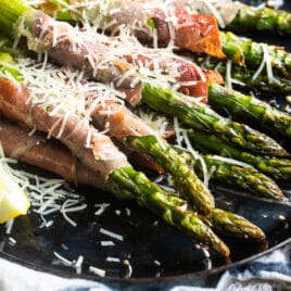 Prosciutto wrapped asparagus on a black plate with shredded Parmesan.