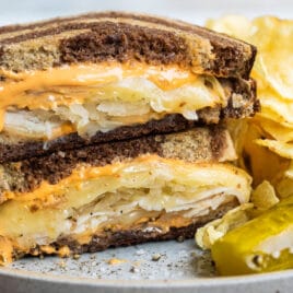 A rachel sandwich on a gray plate with a pickle spear and potato chips.