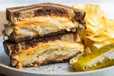 A rachel sandwich on a gray plate with a pickle spear and potato chips.