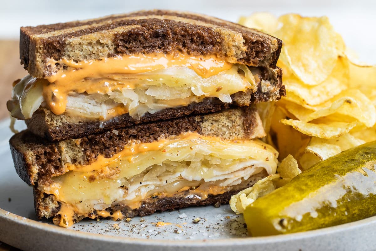 A rachel sandwich on a gray plate with a pickle spear and potato chips.