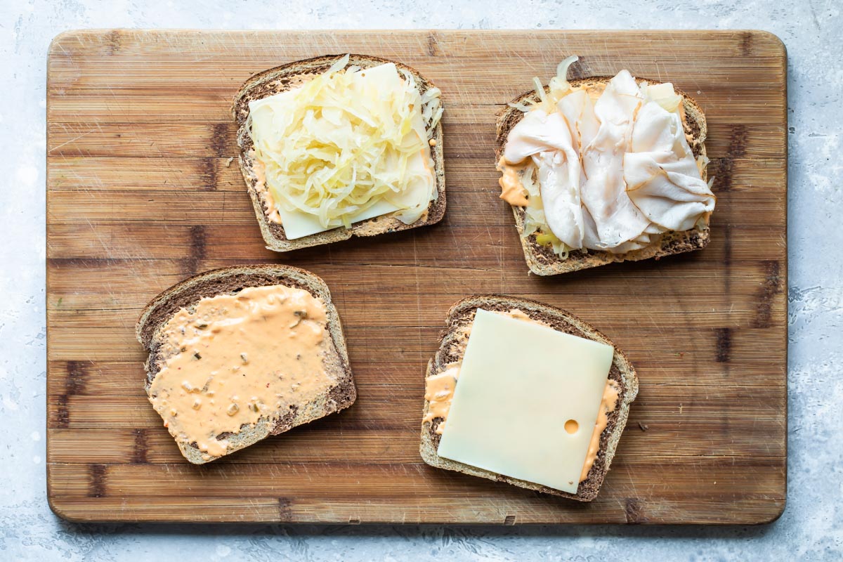 Assembling a rachel sandwich on a cutting board.