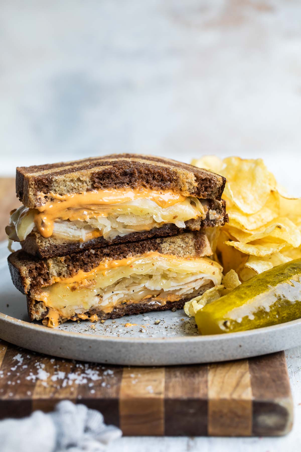 A rachel sandwich on a gray plate with a pickle spear and potato chips.