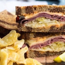 A reuben sandwich on a cutting board surrounded by chips and a pickle spear.