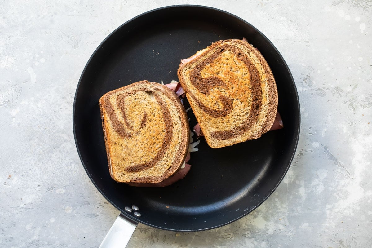 Two reuben sandwiches in a frying pan.