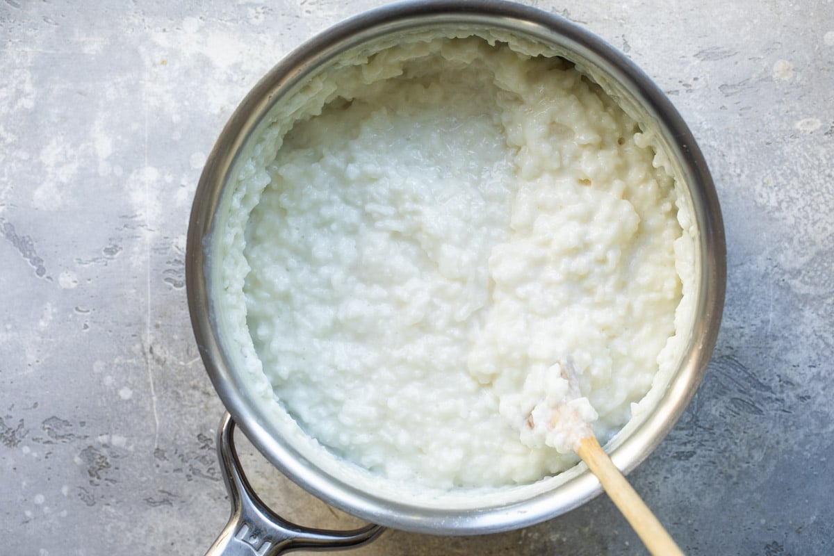 Rice pudding in a silver pot with a wooden spoon.