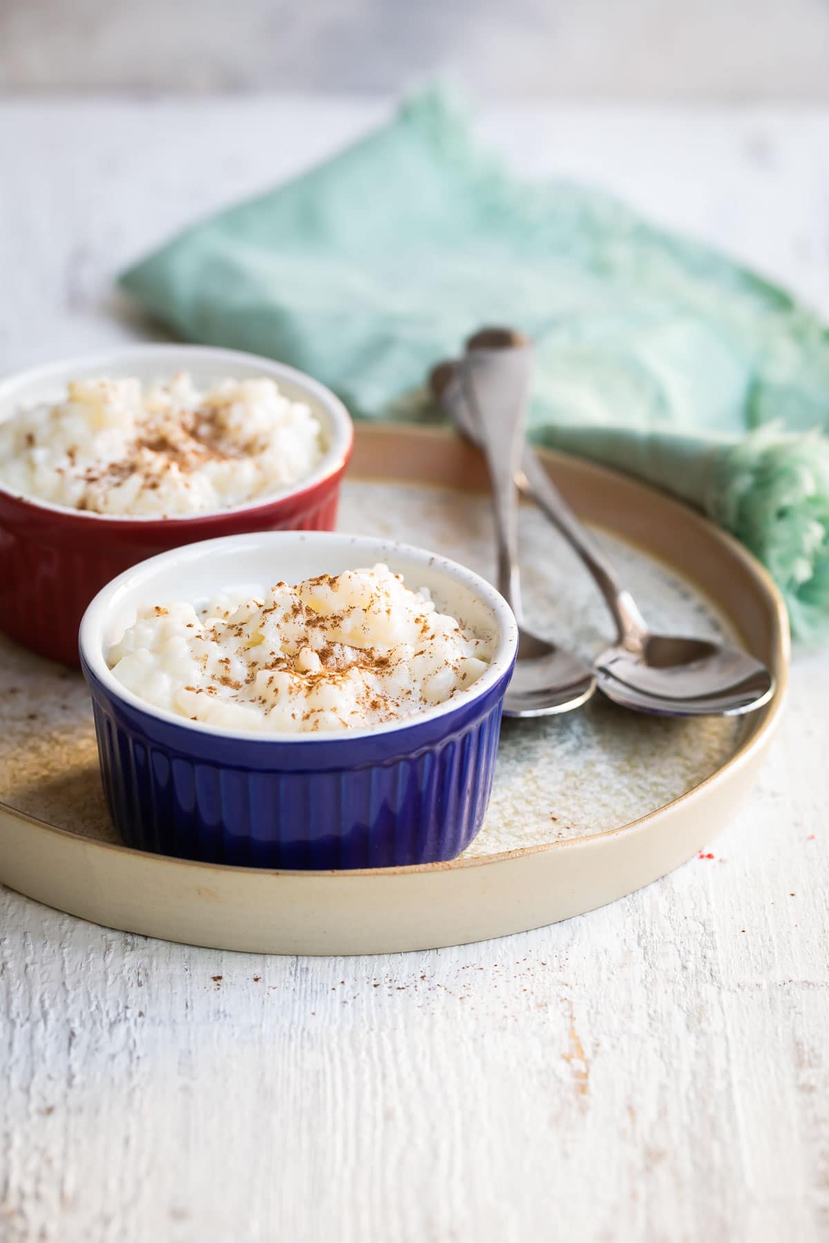 Rice pudding in two ramekins on a plate next to two spoons.