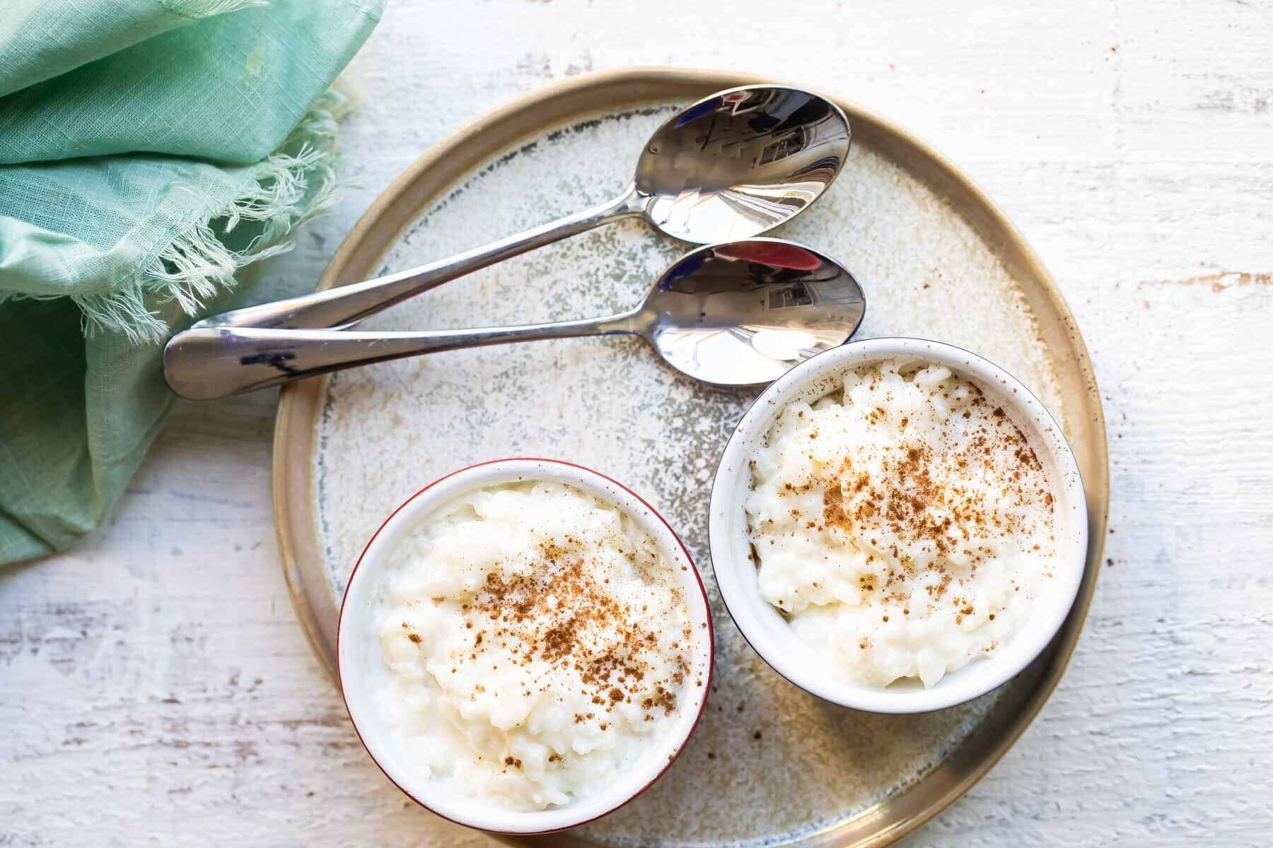Rice pudding in two ramekins on a plate next to two spoons.