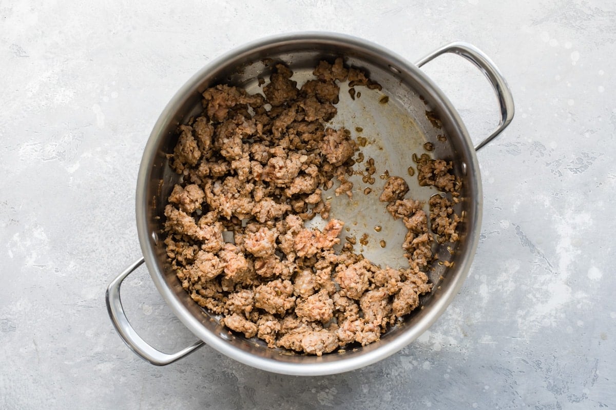 Ground sausage and onion in a silver pot.