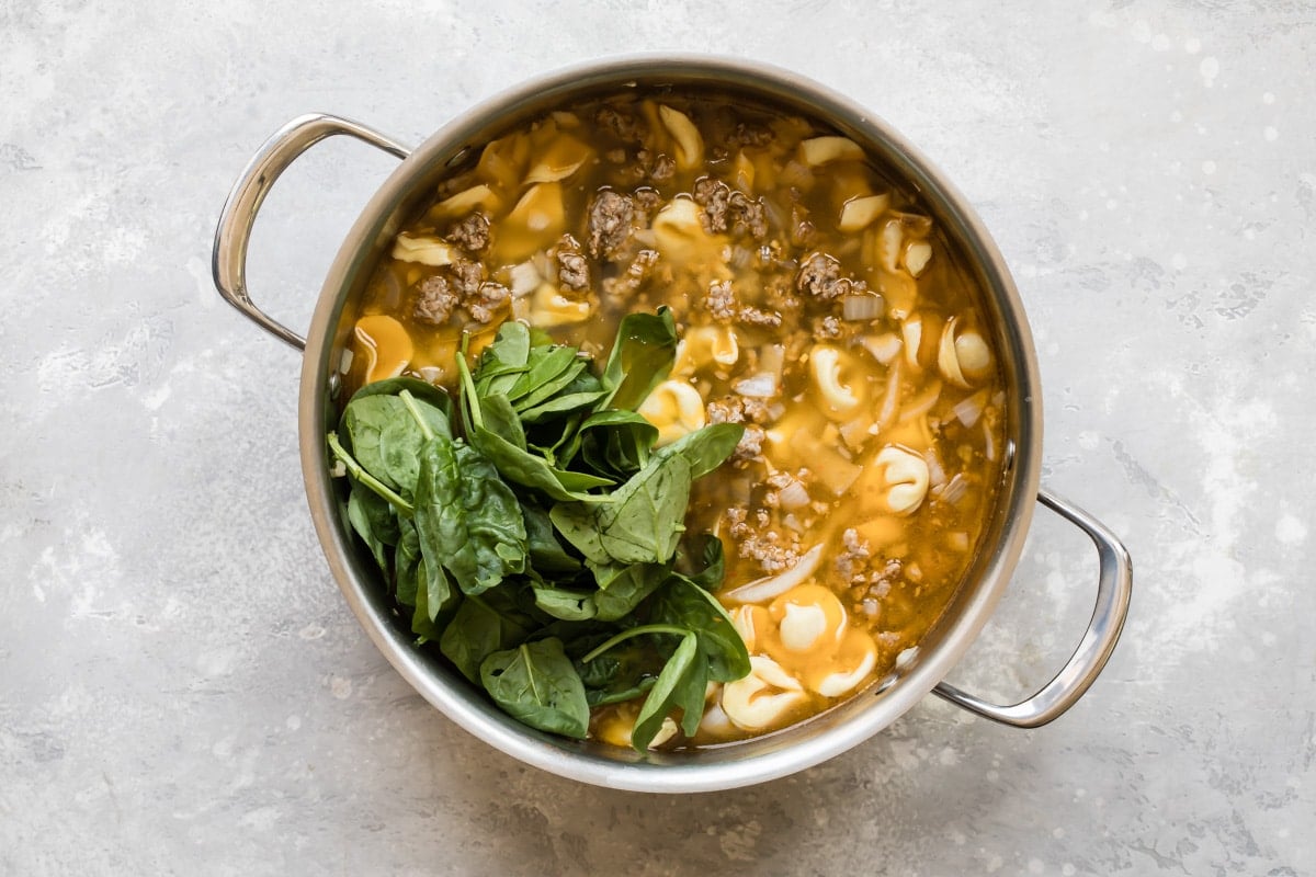 Sausage tortellini soup in a silver pot.