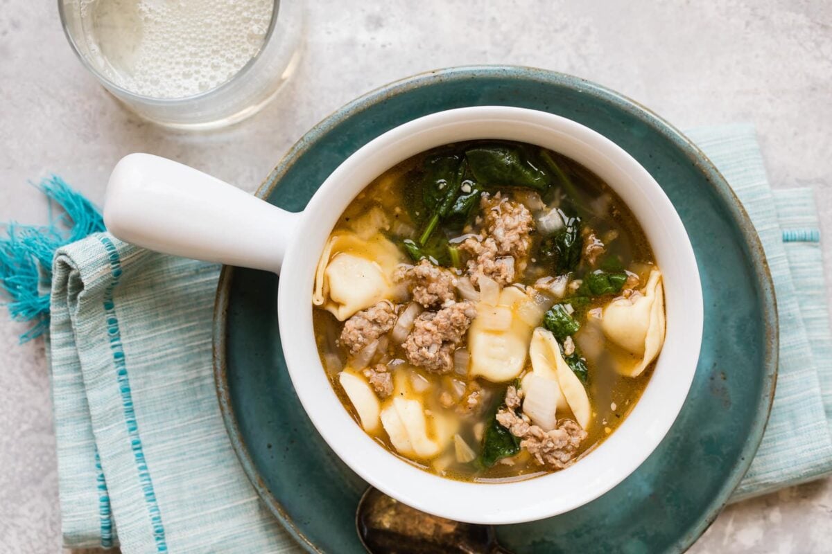 Sausage tortellini soup in a white bowl.