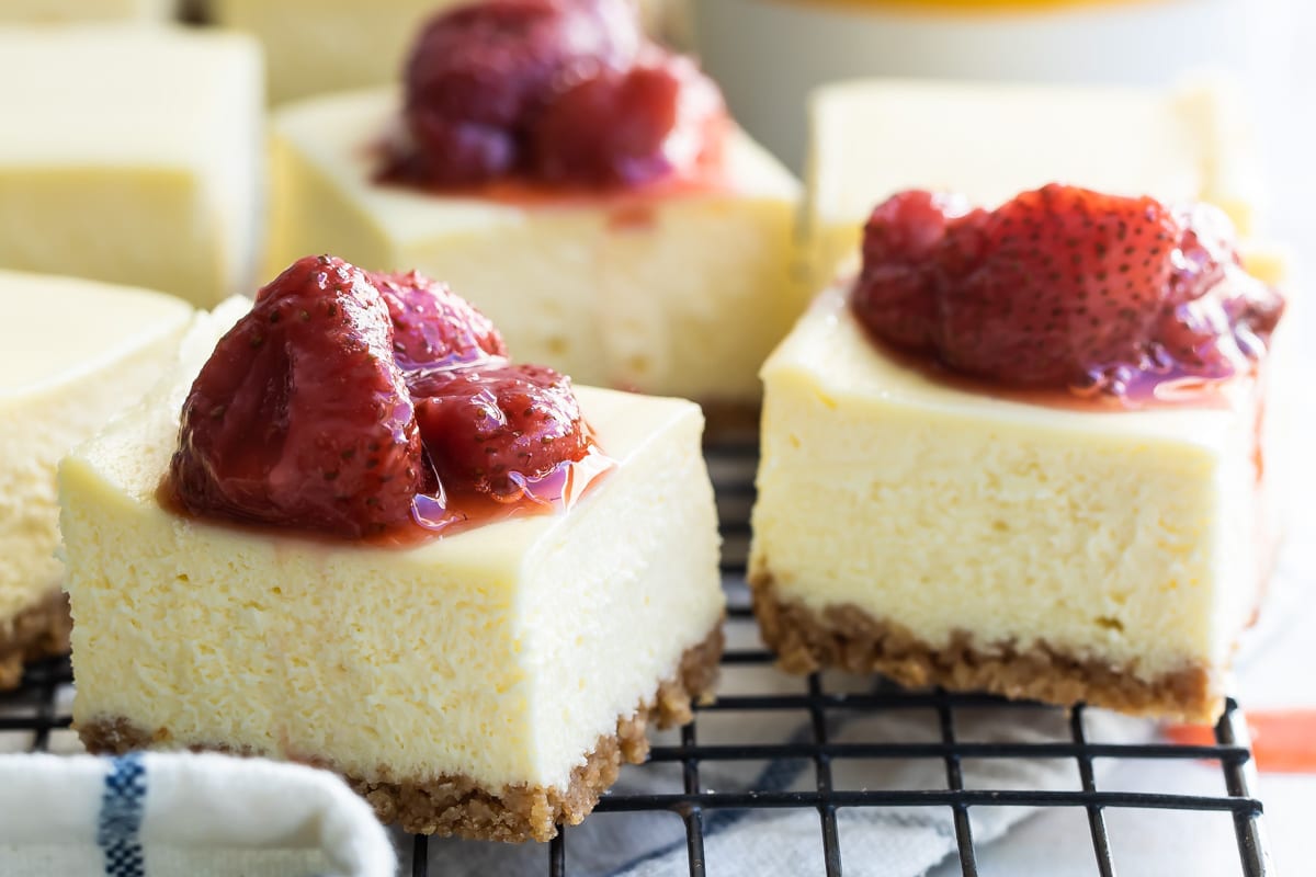 Cheesecake squares topped with strawberry topping on a cooling rack.