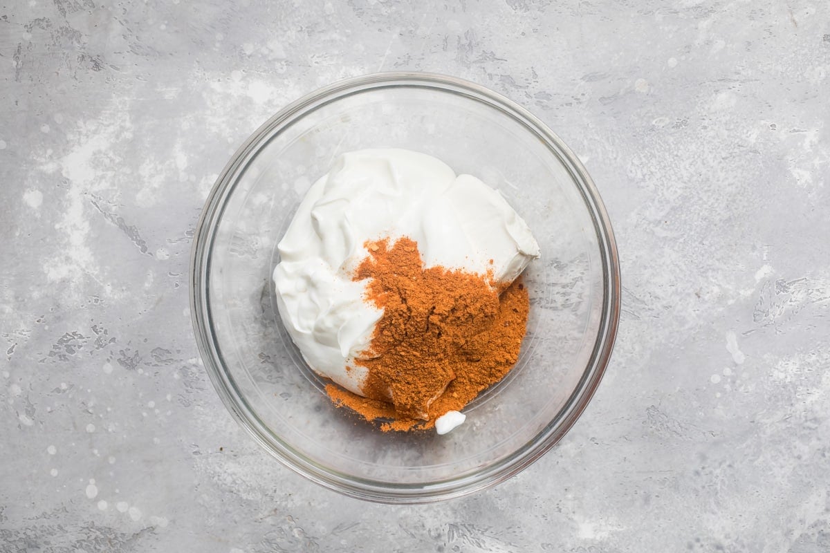 Taco seasoning, cream cheese and sour cream in a clear bowl before being mixed.