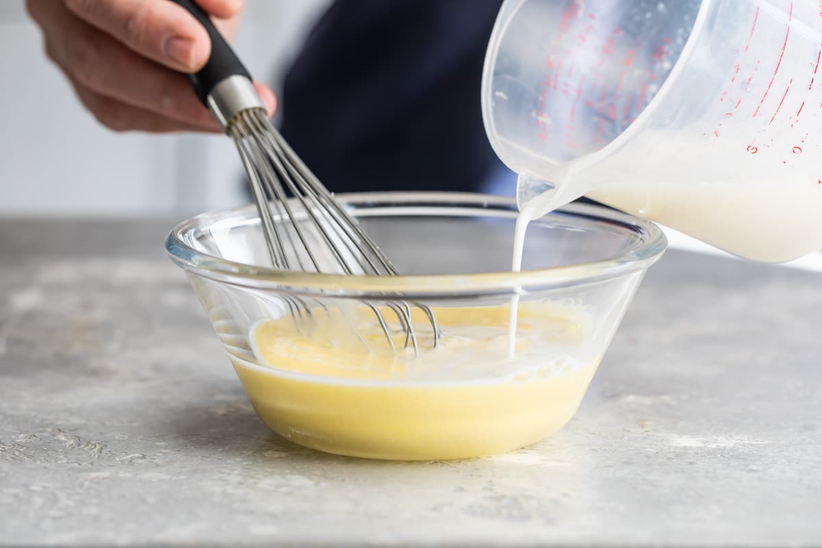 Milk being poured into a creamy yellow mixture.
