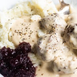 Swedish meatballs on plates with mashed potatoes, gravy, and cranberry sauce.