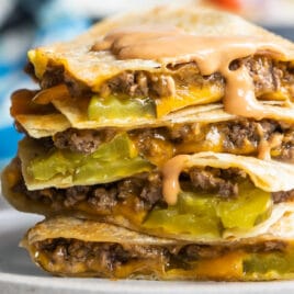 A cheeseburger quesadilla stacked on a plate with a wedge salad in the background.